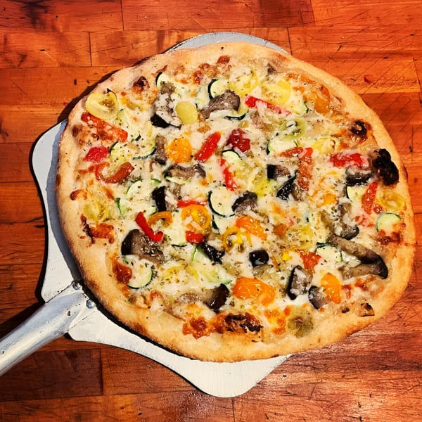 Farm Star Pizza's vegetarian pizza with zucchini, peppers, and mushrooms on a pizza peel.