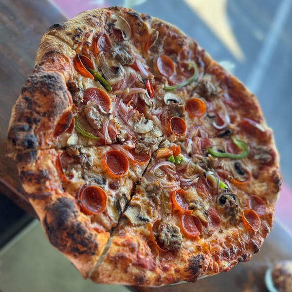 Close-up of a whole pizza with pepperoni, mushrooms, onions, and green peppers on a wooden table.