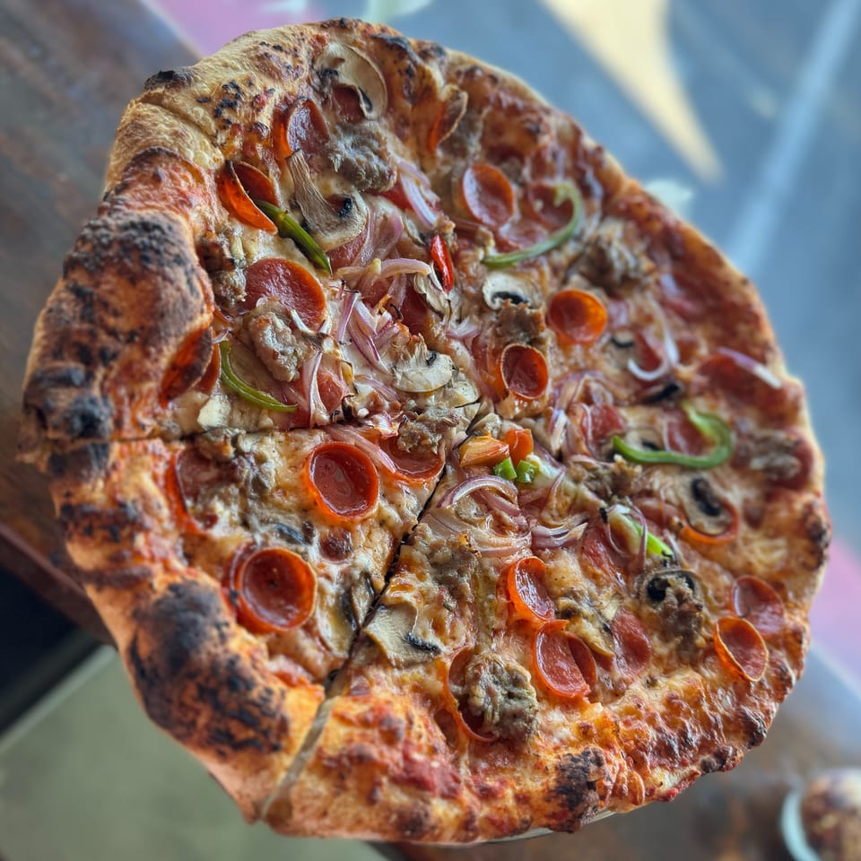 Close-up of a whole pizza with pepperoni, mushrooms, onions, and green peppers on a wooden table.