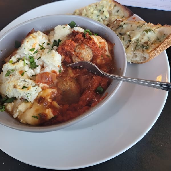 A bowl of Italian meatballs with ricotta cheese and marinara sauce, served with garlic bread.