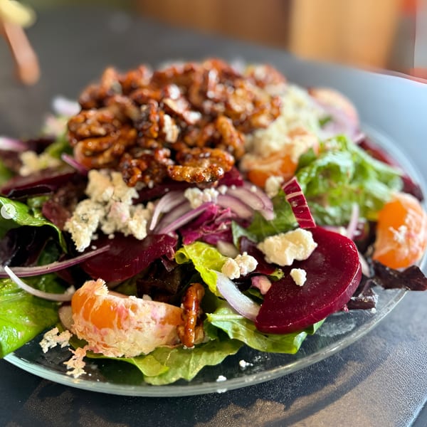 A vibrant salad with candied walnuts, beets, red onion, feta, and mandarin oranges on a clear plate.