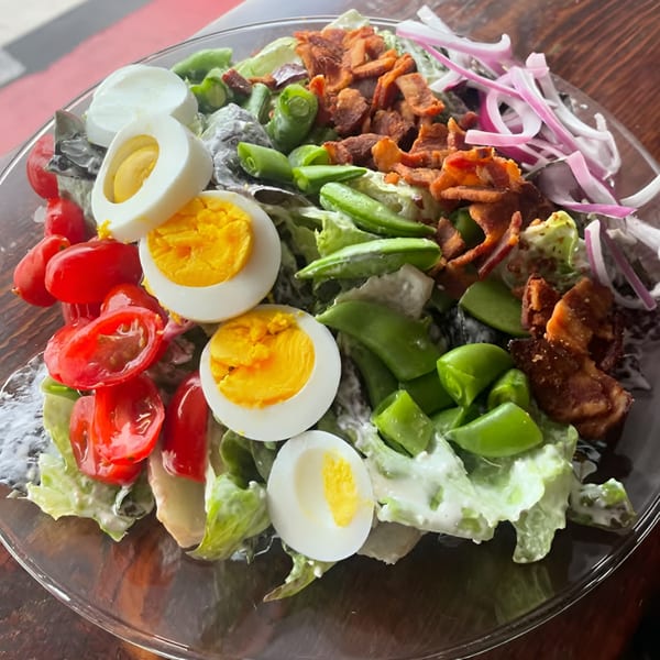 A vibrant salad with lettuce, cherry tomatoes, hard-boiled eggs, bacon, and red onion.