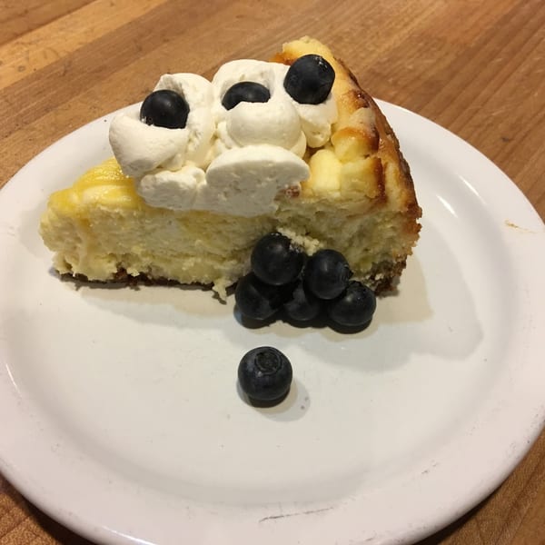 A slice of cheesecake topped with whipped cream and blueberries on a white plate.